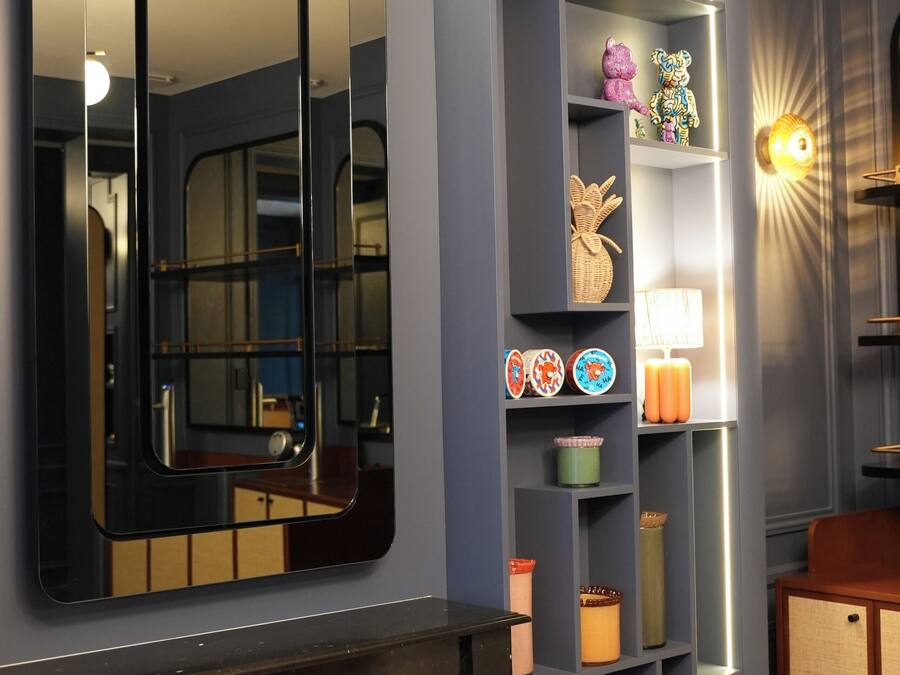 Un intérieur moderne agrémenté d’un grand miroir, d’étagères ornées d’objets décoratifs et d’un luminaire fixé au mur.