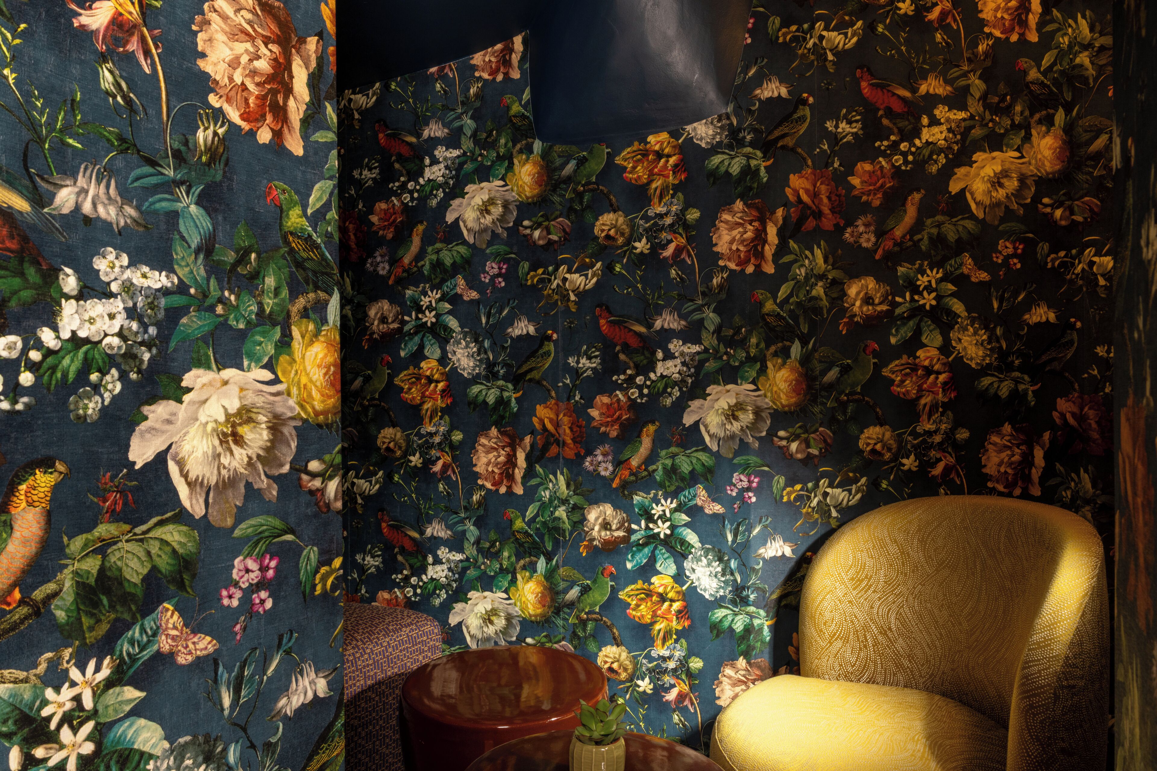 Een kamer met bloemenbehang, een gouden fauteuil en een klein houten tafeltje.
