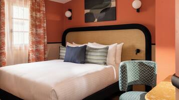 Habitación de hotel con cama, una silla, una obra de arte en la pared y una ventana con cortinas.