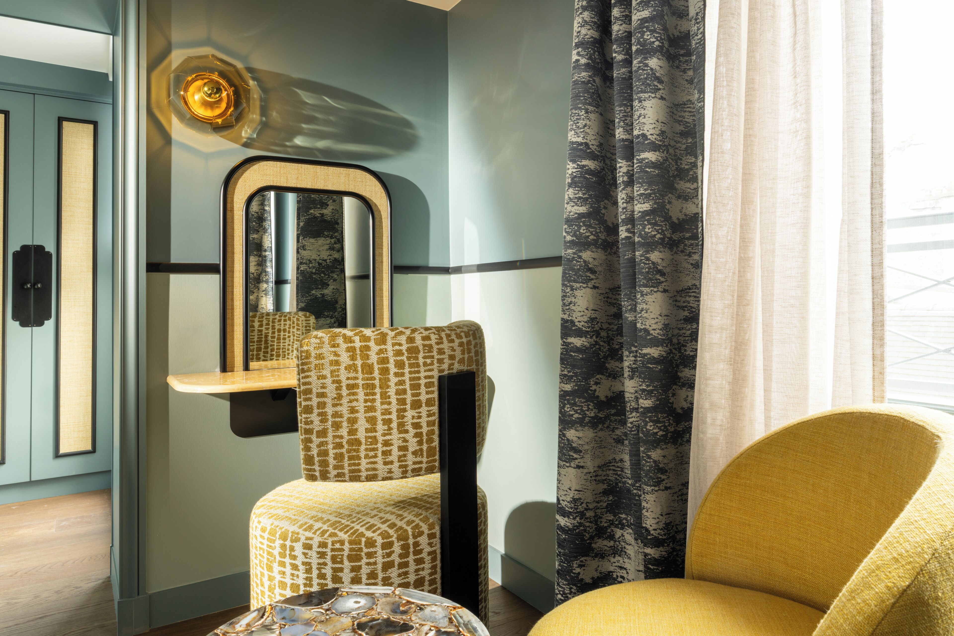 Una habitación con un sillón estampado, un espejo y una ventana con cortinas.