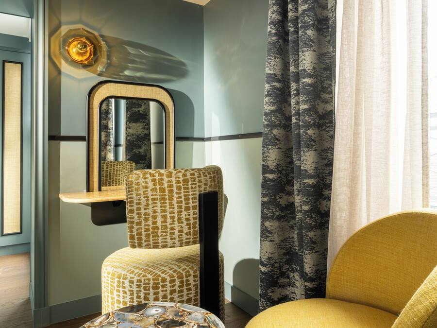 Una habitación con un sillón estampado, un espejo y una ventana con cortinas.