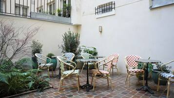 A courtyard with tiled flooring, wicker chairs, and potted plants.
