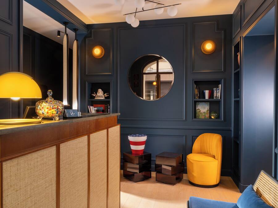 Una habitación con una recepción, un sillón amarillo, un espejo redondo y una estantería.