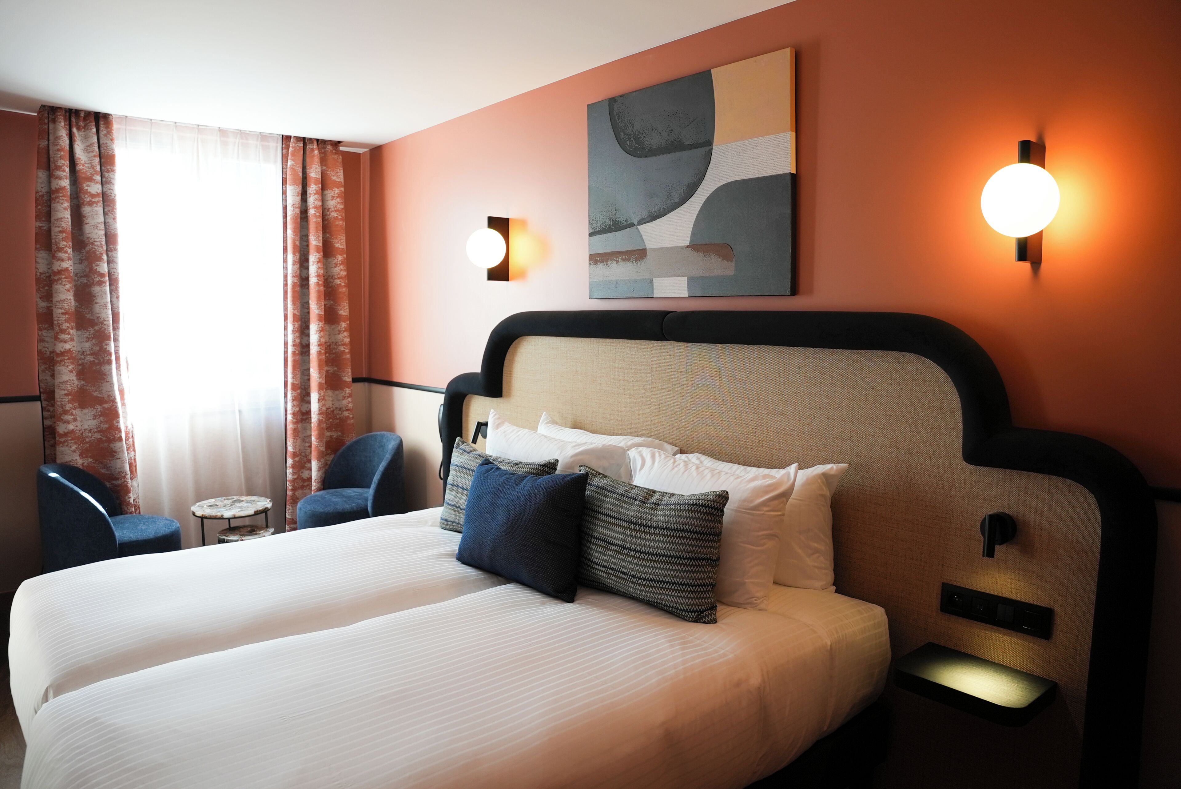 A hotel room with a large bed, two bedside tables, a nightstand, a chair, a small table, and a painting on the wall.
