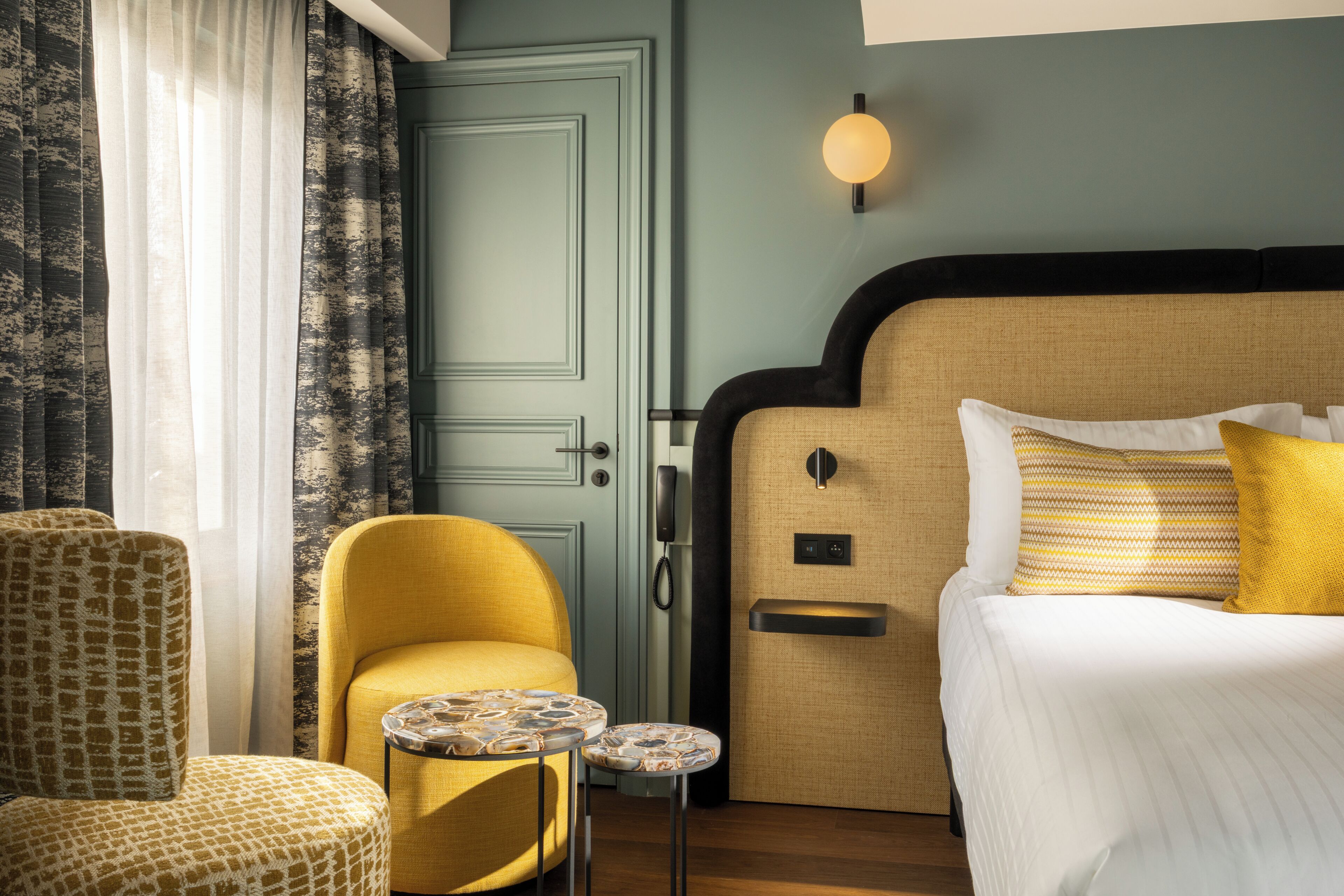 A hotel room with a bed, a chair, a small table, and a door.