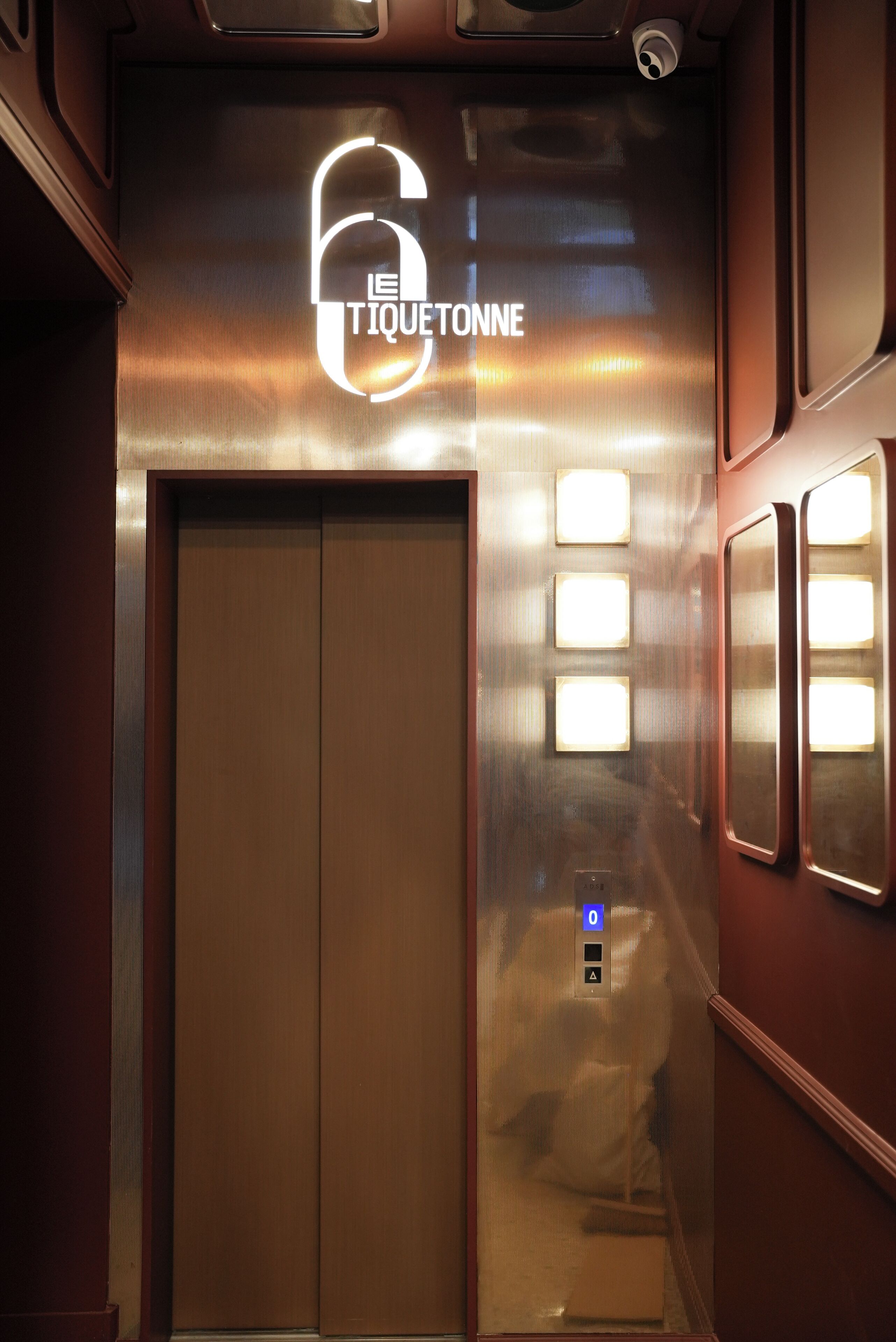 An elevator with a sign reading '6 LE TIQUETONNE' and illuminated buttons.