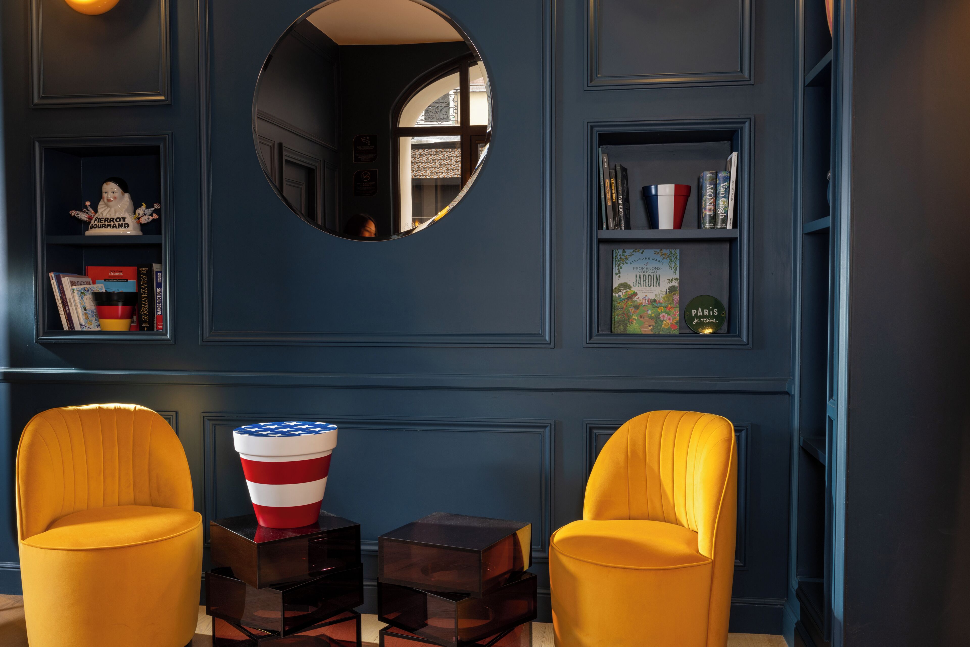 A room with two yellow chairs, a mirror, a bookshelf, and a small American flag decoration.