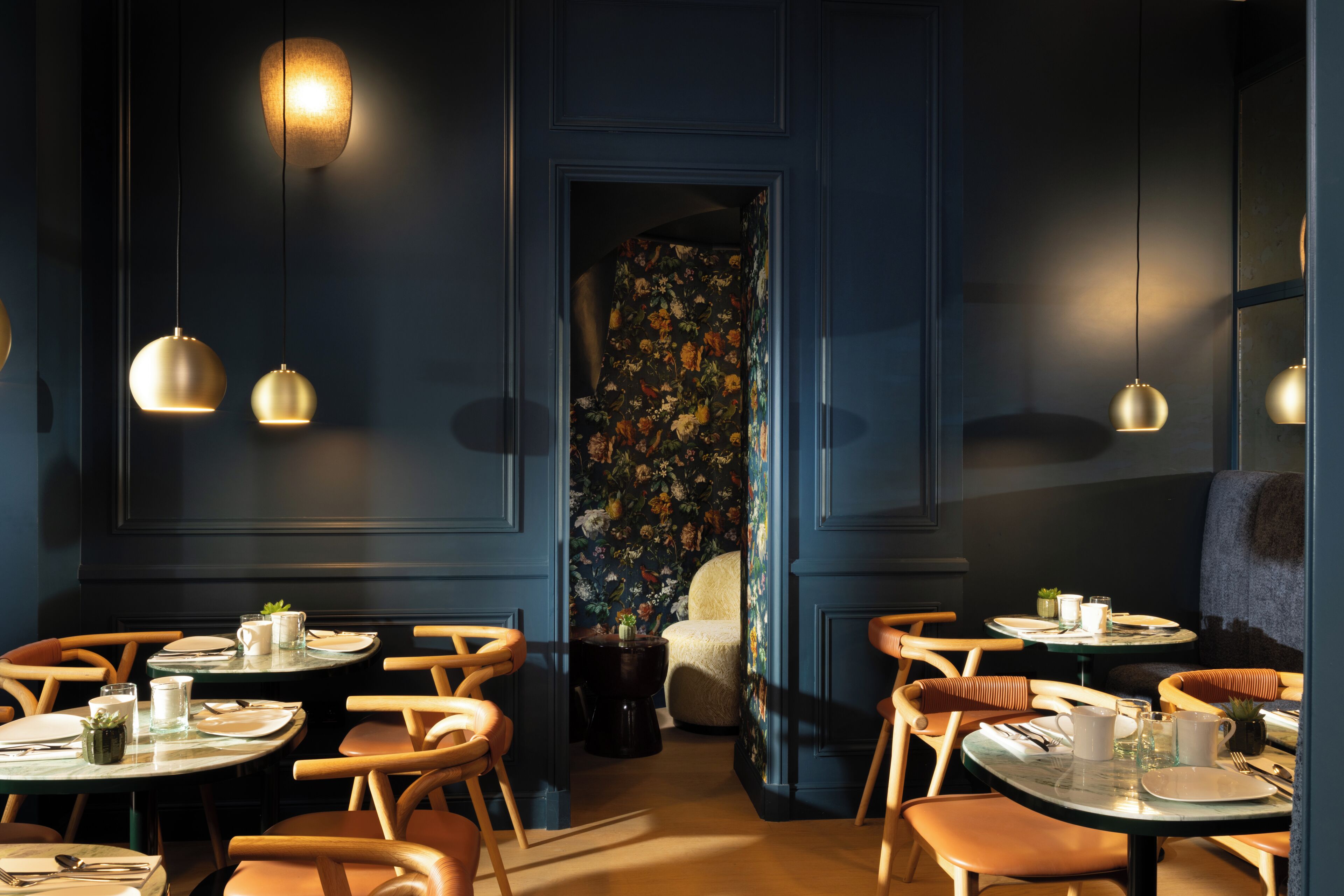 A restaurant with round tables, wooden chairs, and hanging pendant lights.