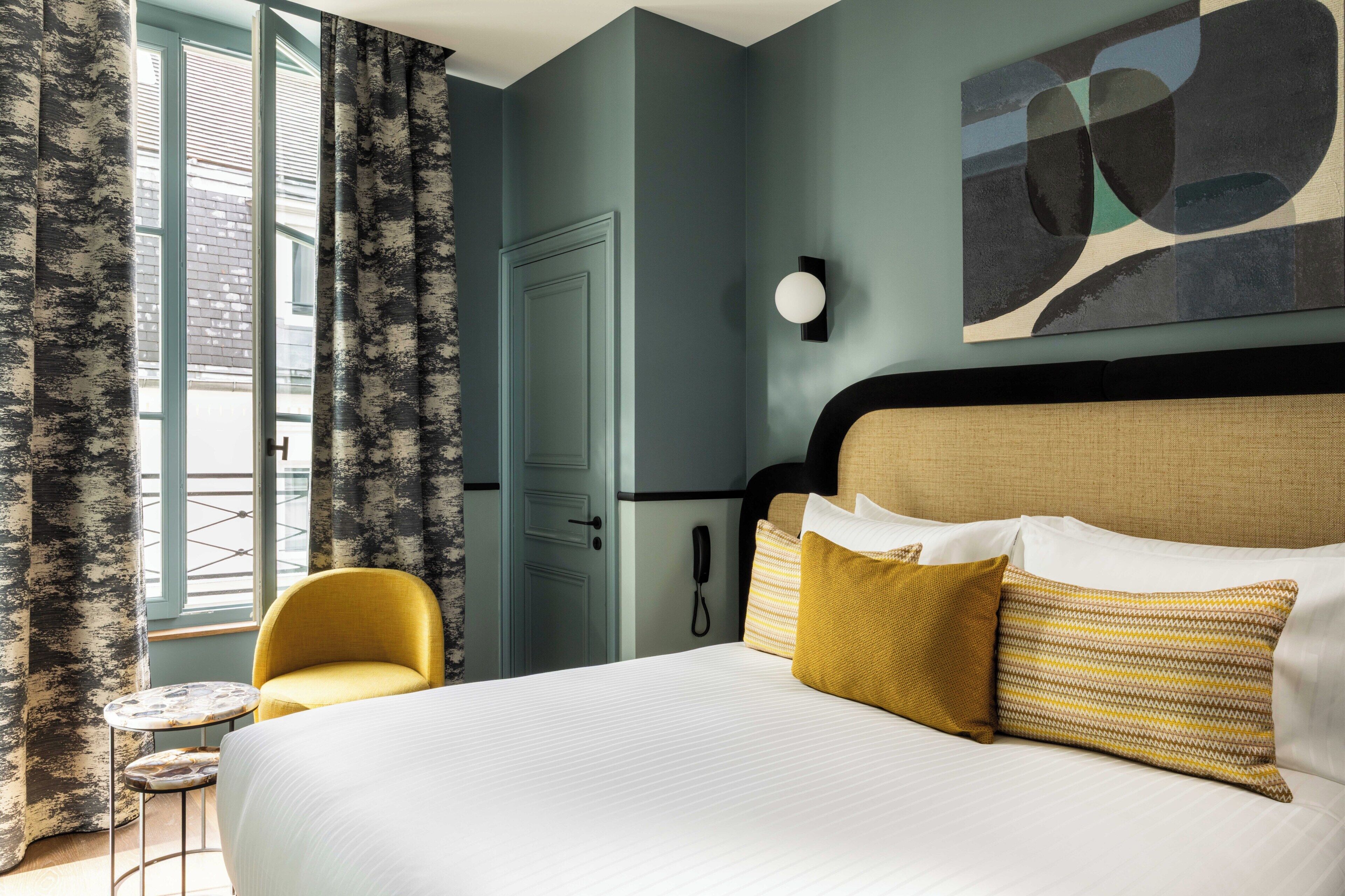 Una habitación de hotel con cama, una silla, una mesita, teléfono y ventana con cortinas.