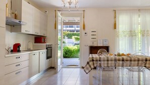 A modern kitchen with a dining area, featuring a checkered tablecloth, clear chairs, and a view of greenery outside. - Apartment "Betty's House" with Pool, Wi-Fi, and Air Conditioning (Cavalcaselle)