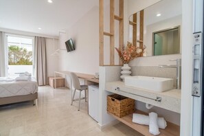 A modern hotel room with a large bed, a desk, a flat-screen TV, a large mirror, a white sink, and a small refrigerator. - Zante Apts (Laganas)