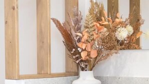 A bathroom with a white sink, a white vase with dried flowers, and wooden paneling on the wall. - Zante Apts (Laganas)