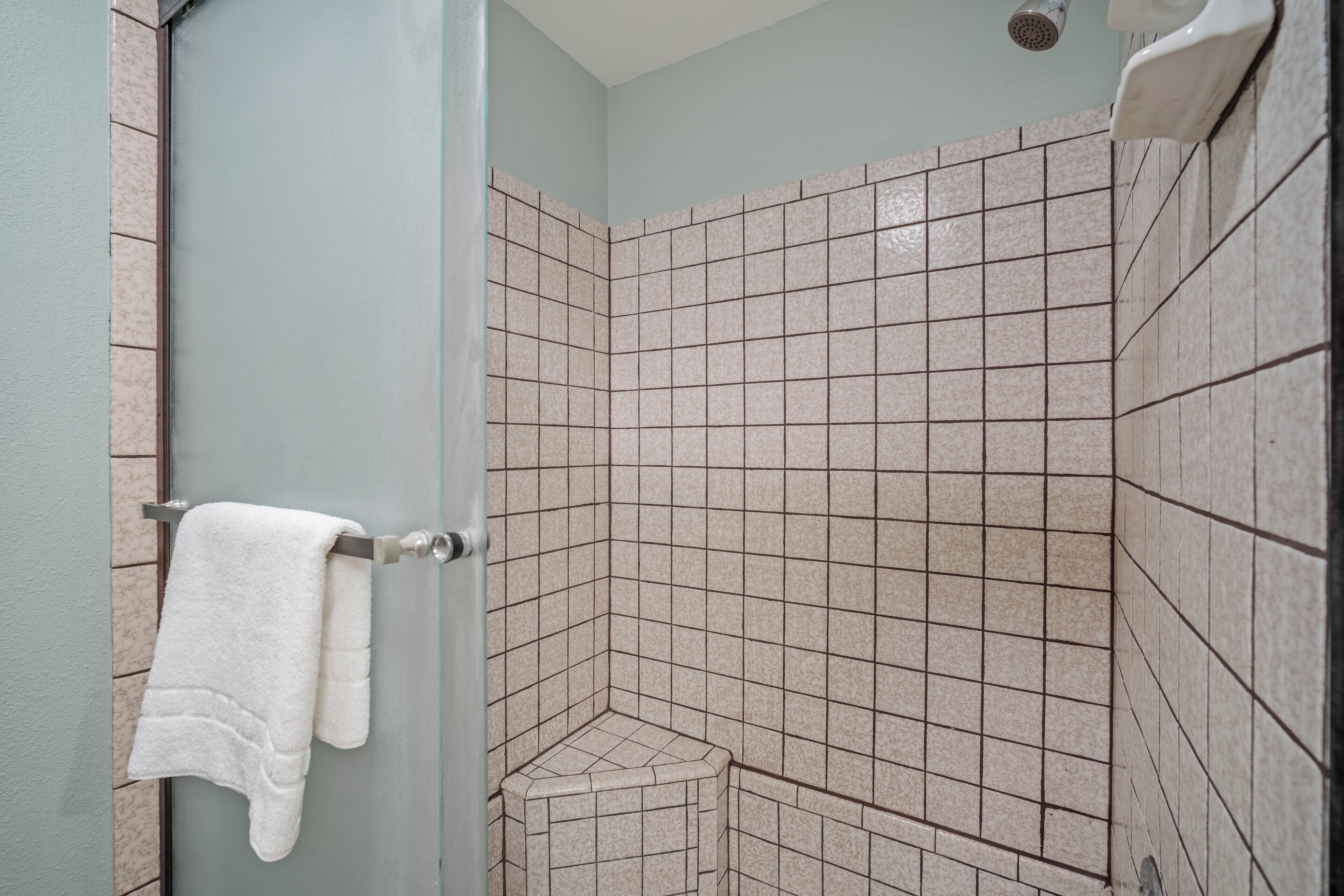 A bathroom with a tiled shower area, a towel rack, and a corner sink.