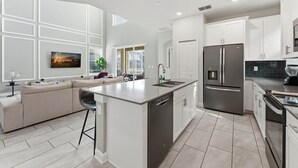 A modern kitchen with a central island, white cabinetry, stainless steel appliances, and a large window providing natural light.
