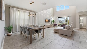 A spacious living area with a dining table, sofa, and large windows.