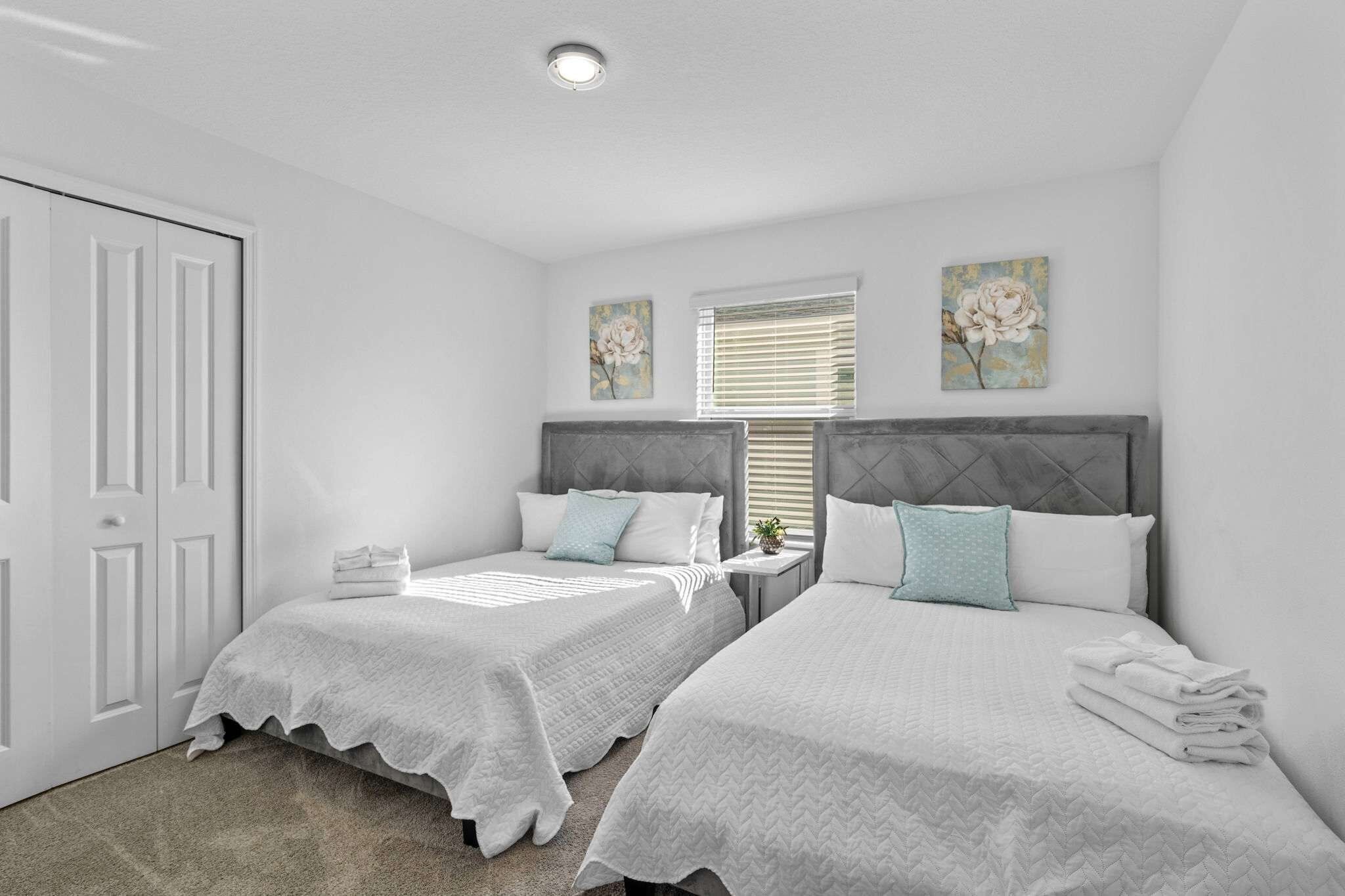 A bedroom with two beds, a window with blinds, and a door.