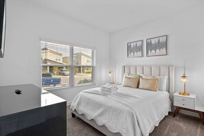 A bedroom with a bed, bedside tables, a window with blinds, and artwork on the wall.