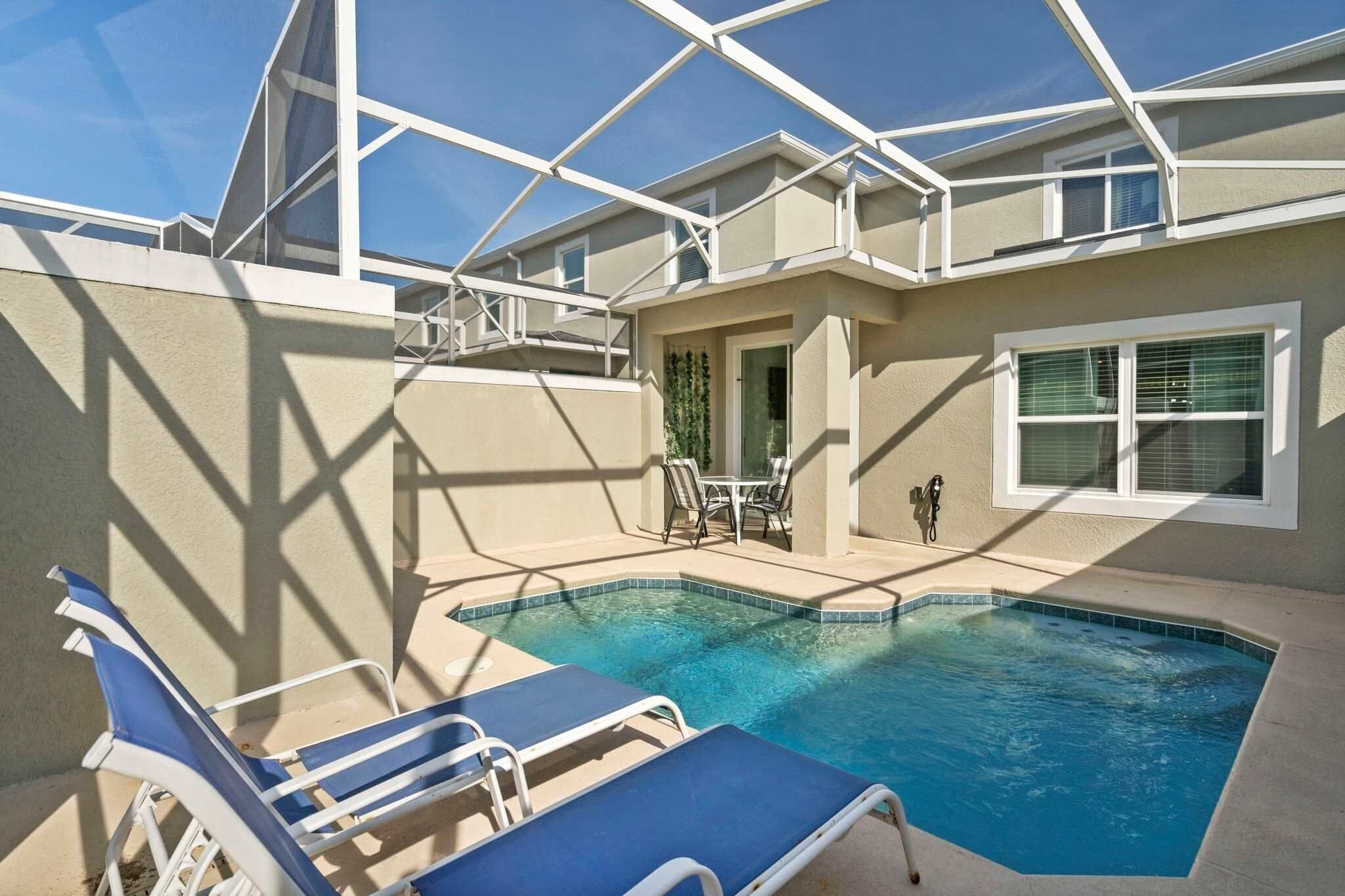 A swimming pool with lounge chairs, a covered patio, and a view of the sky.