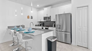 A modern kitchen with white cabinets, stainless steel appliances, and a central island with bar stools. - 5BR Townhome w/ Pool at Champions Gate (Kissimmee)