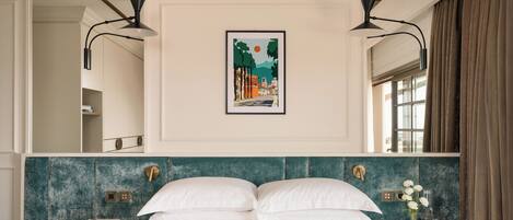 A bedroom with a bed, two bedside tables, a nightstand, a framed picture, and a window with curtains.