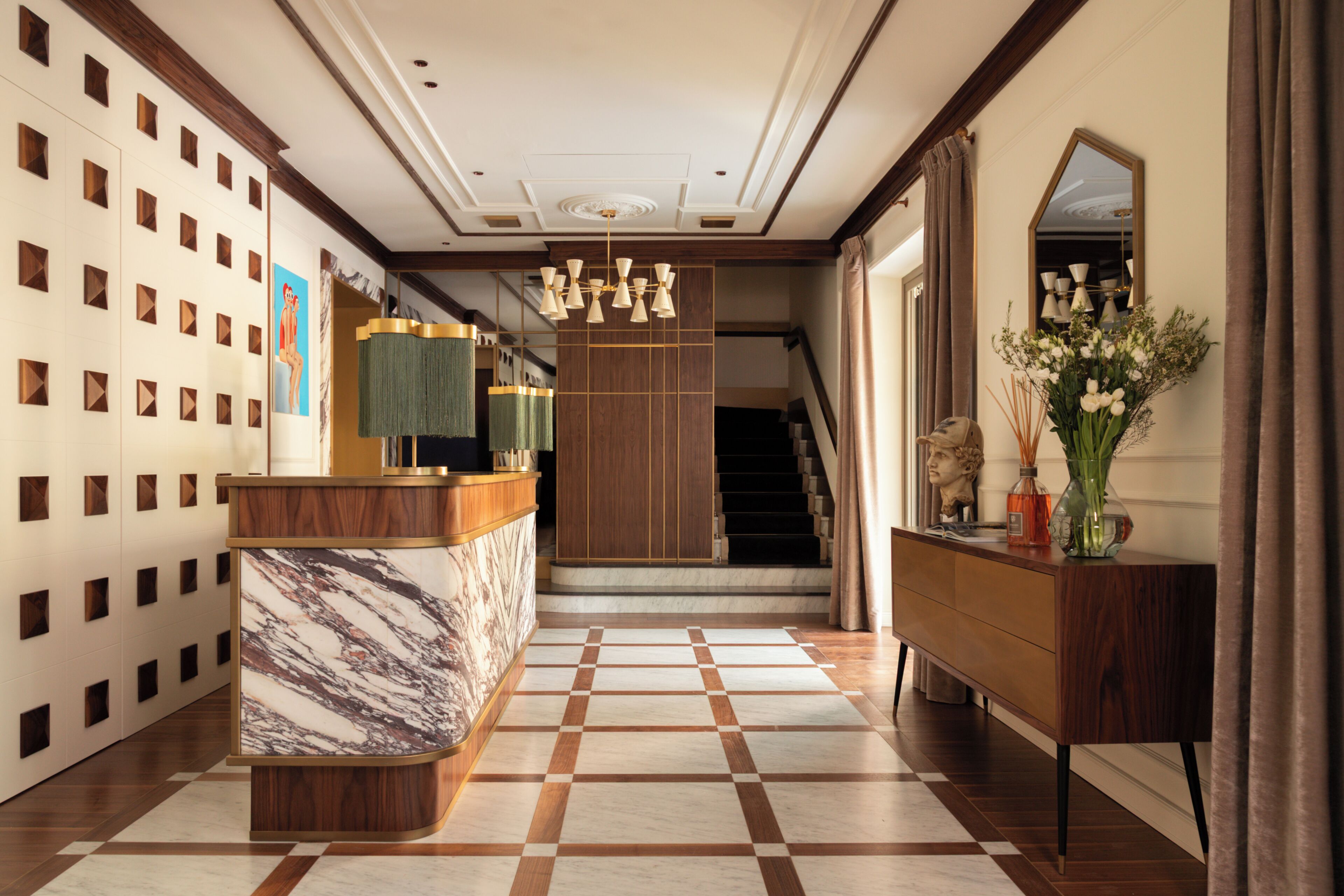 Un hall d’hôtel avec un comptoir de réception en marbre, un escalier et un meuble en bois orné d’un vase de fleurs.