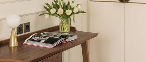 A wooden table with a vase of white flowers, a book, and a lamp.