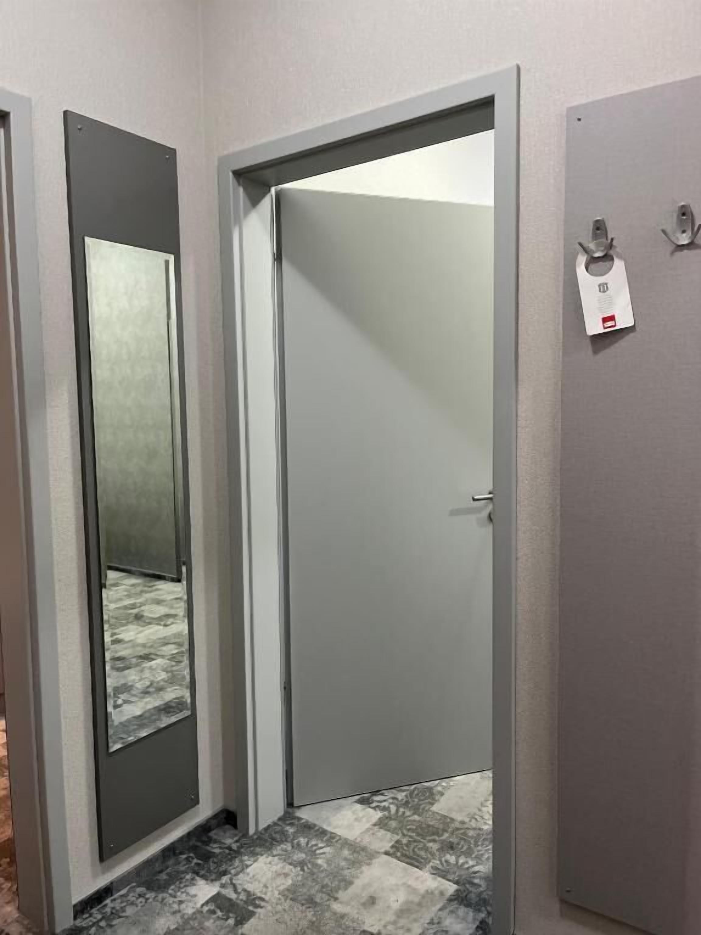 A hallway with a closed door, a mirror, and a coat hook with a tag.