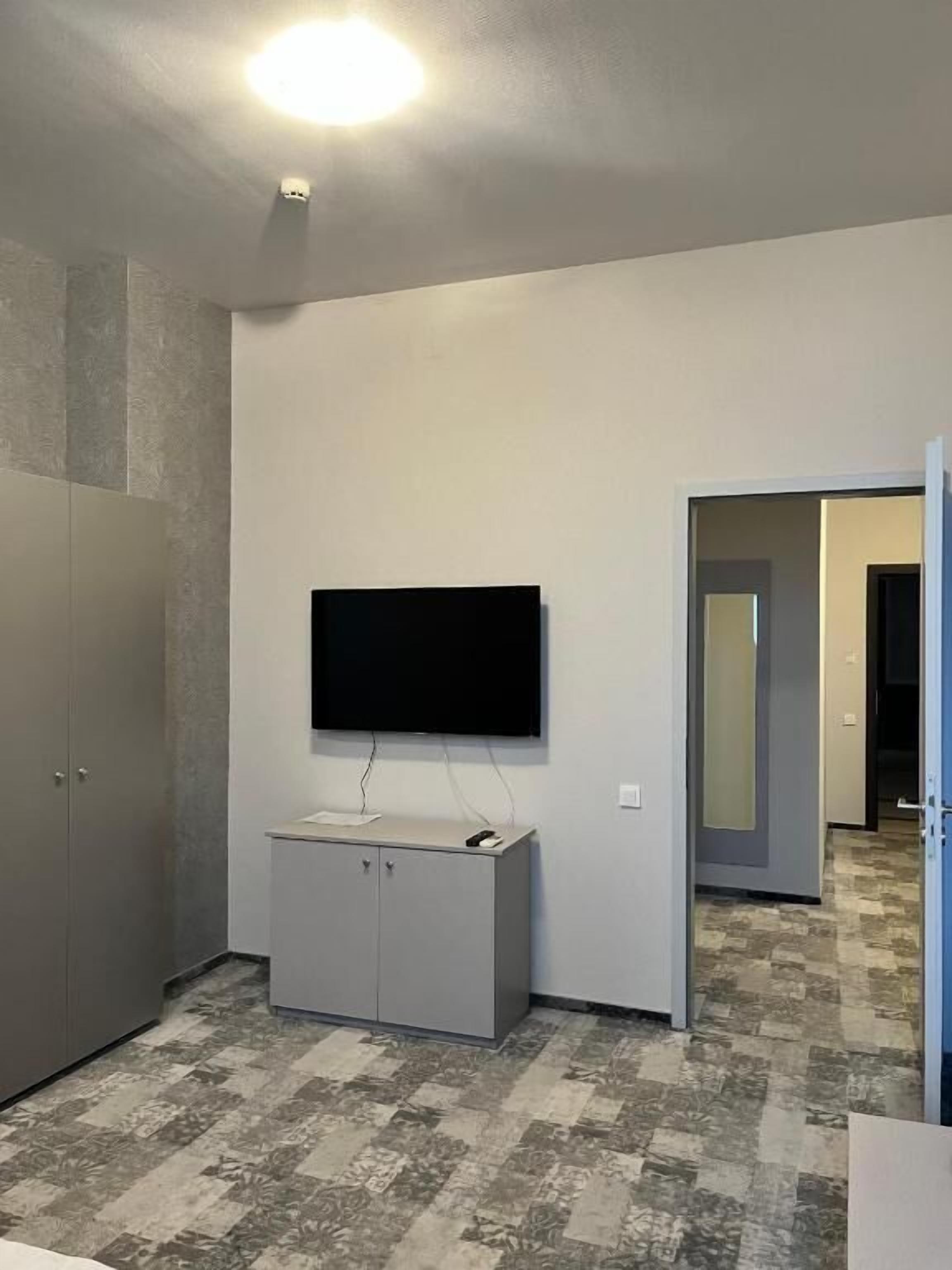 Una habitación con televisión de pantalla plana montada en la pared, un mueble gris y suelo estampado.