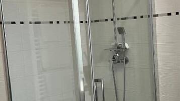 Baño con cabina de ducha acristalada, cabezal de ducha de mano y grifo empotrado.