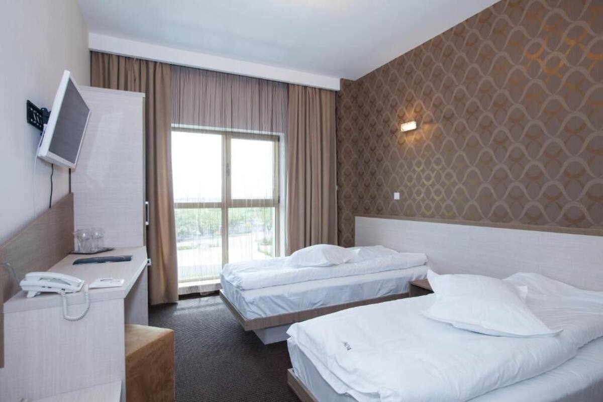 Habitación de hotel con dos camas, un escritorio con teléfono, televisión montada en la pared y un gran ventanal con cortinas.