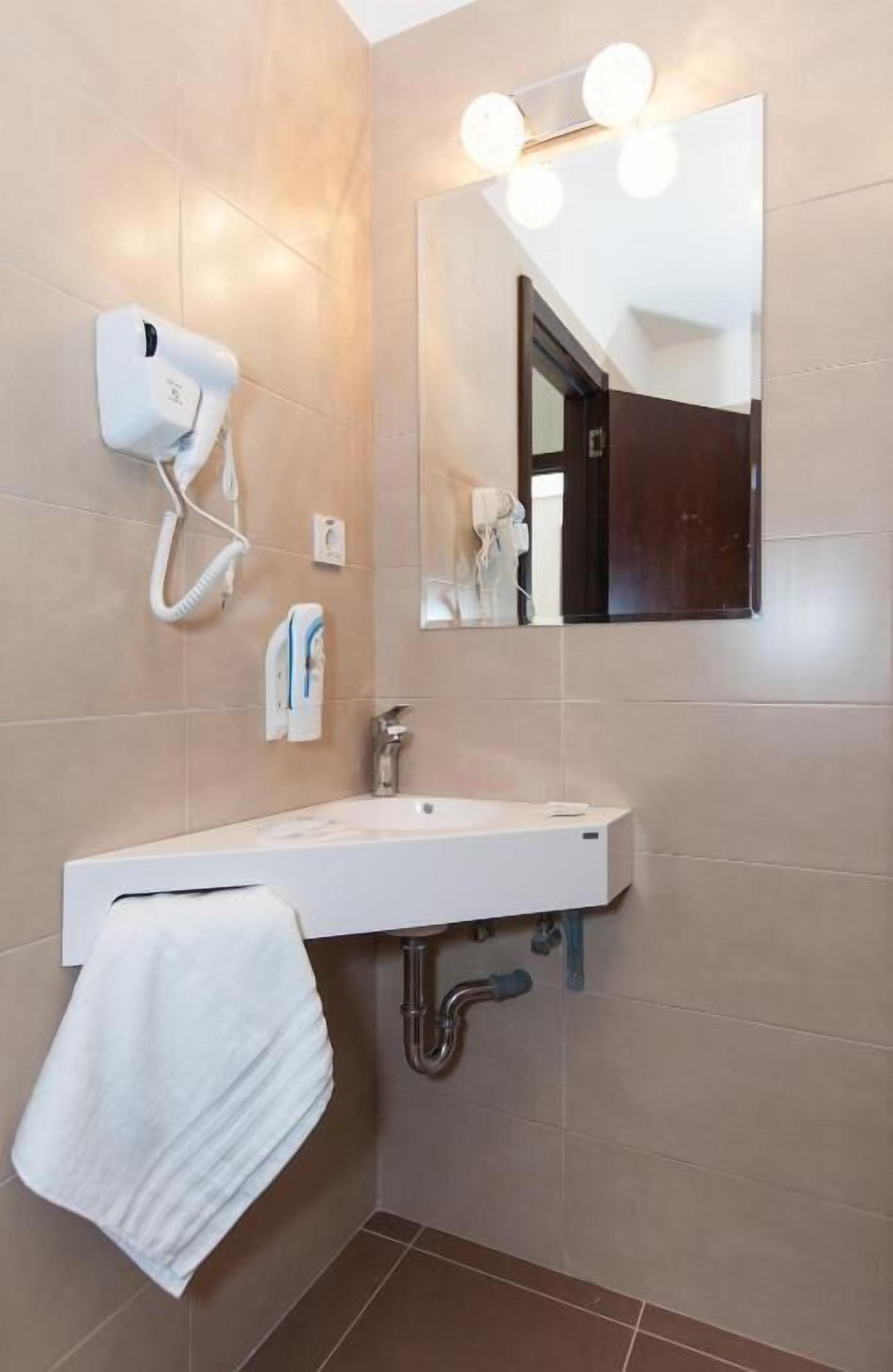 A bathroom with a white sink, a towel hanging on the wall, a hairdryer, and a mirror with lights.