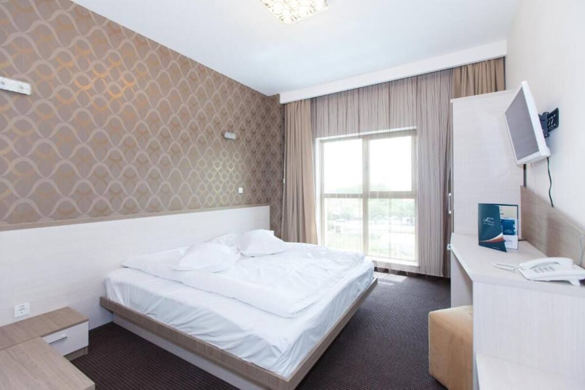 Habitación de hotel con cama, escritorio con computadora, televisor y ventana con cortinas.