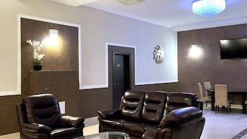Un área de descanso moderna con sofás de cuero, una mesa de centro de vidrio y un televisor de pantalla plana montado en la pared.
