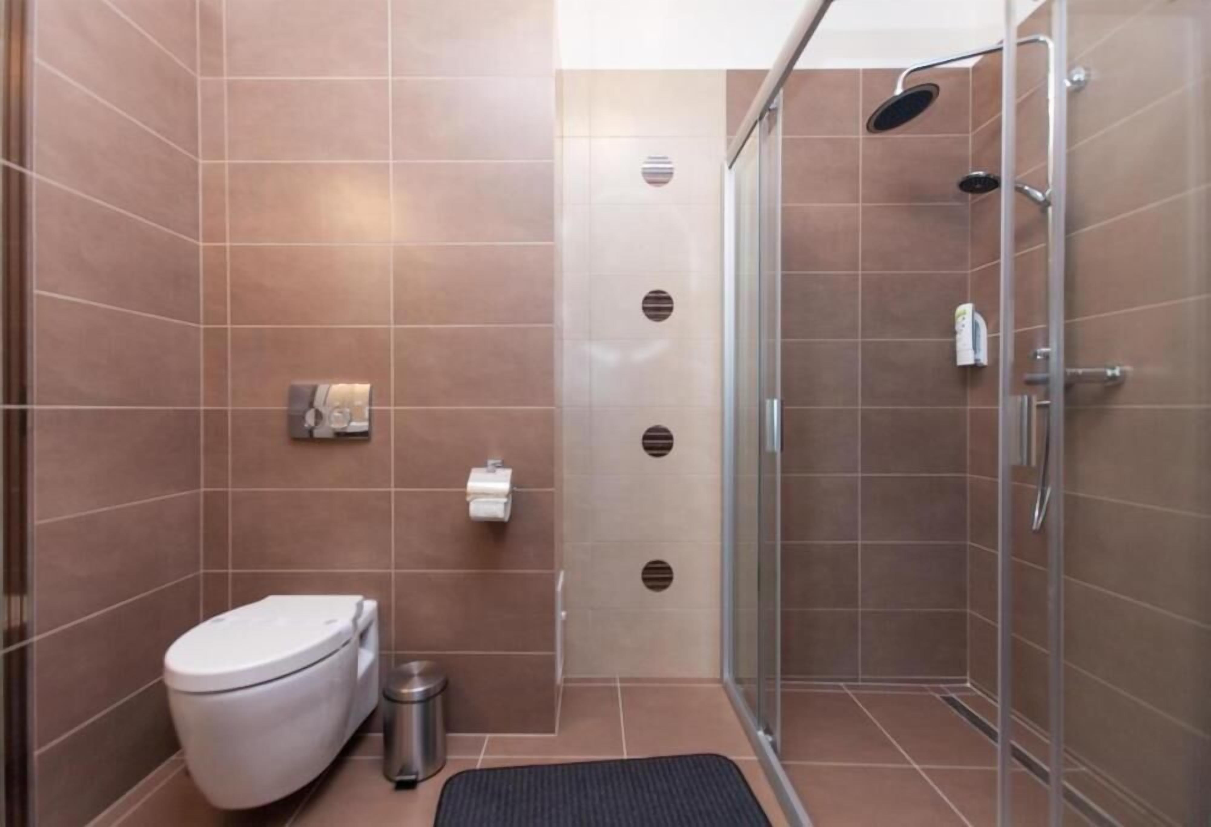 A modern bathroom with a toilet, a trash bin, a shower with a glass door, and a towel rack.