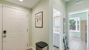 A hallway with a white door, a trash bin, a framed botanical print, and a view of a bathroom with a window. - 1bd/1ba Sunnyvale Suite w/ Private Fenced Patio (Sunnyvale)