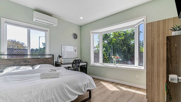 A modern bedroom with a large bed, a desk, and a window with a view of greenery. - 1bd/1ba Sunnyvale Suite w/ Private Fenced Patio (Sunnyvale)
