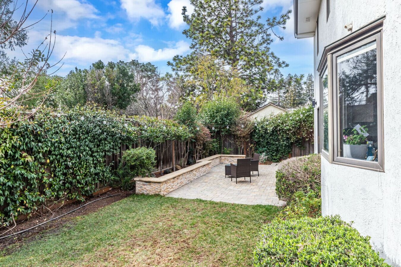 A backyard with a patio, a wooden fence, and a house.