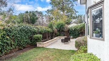 A backyard with a patio, a wooden fence, and a house.