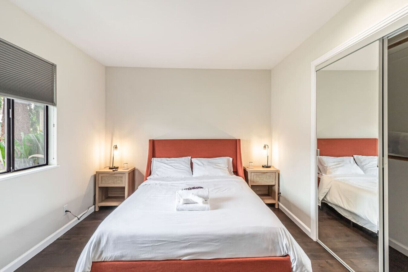 Une chambre d’hôtel avec un grand lit, deux tables de chevet, une fenêtre et un miroir.
