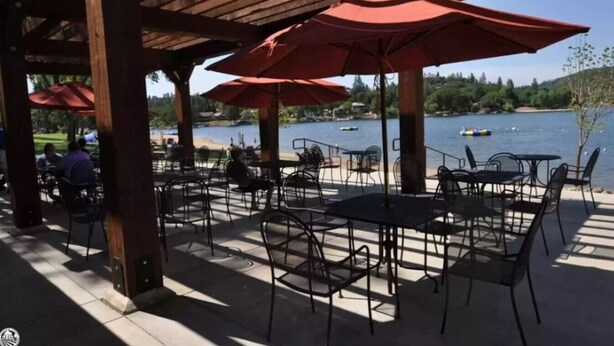 An outdoor patio with tables and chairs, red umbrellas, and a view of a lake with boats. - Big Yosemite Mansion Large Groups Pinemt Lake (Groveland)