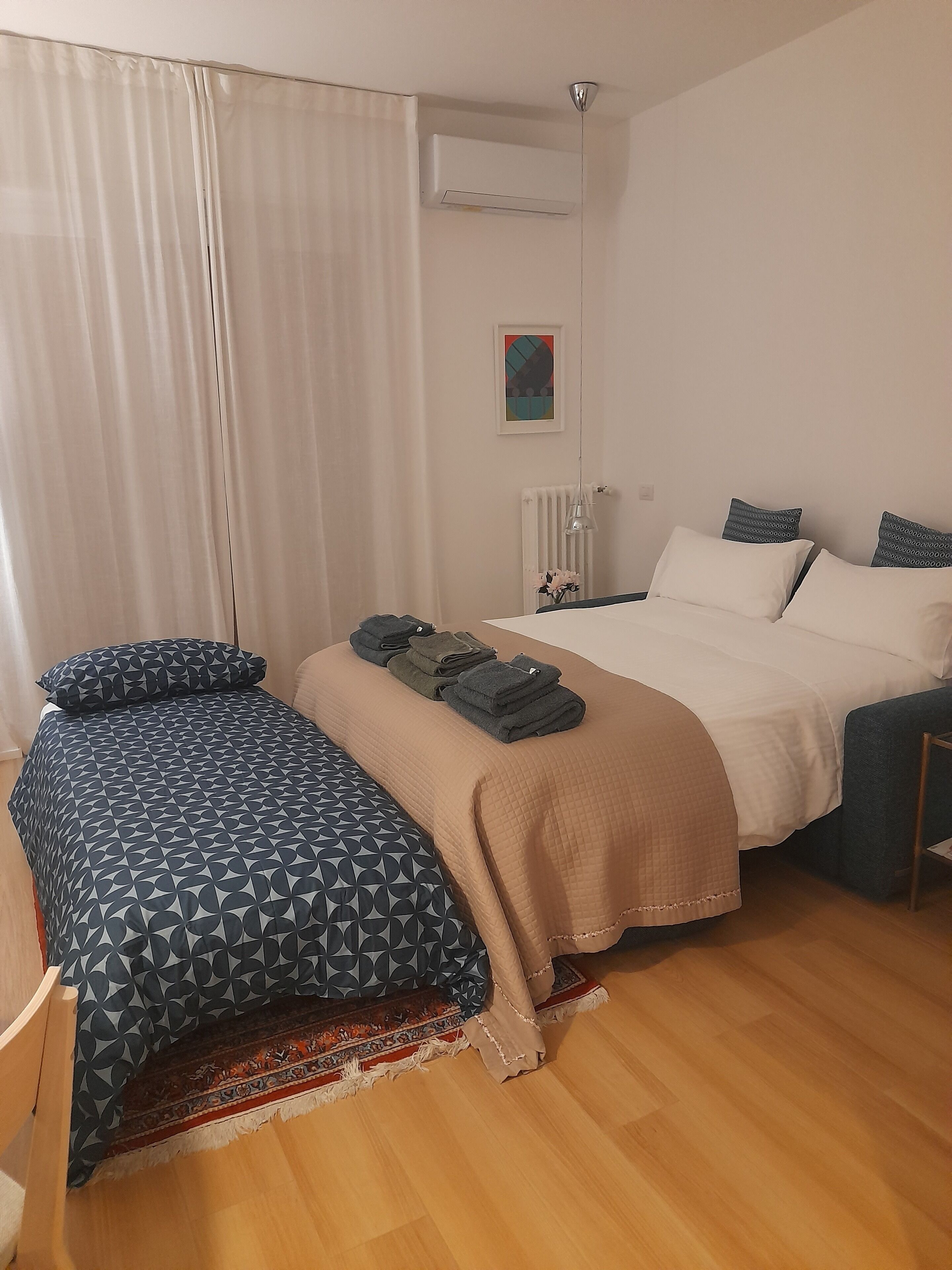 Ein Schlafzimmer mit einem Bett, einem Schreibtisch, einem Stuhl, einem Heizkörper und einem fenster mit Vorhängen.