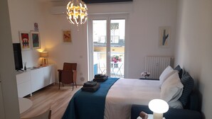 Une chambre d’hôtel avec un lit, un bureau, une chaise, une petite table avec une lampe et un balcon agrémenté de fleurs.