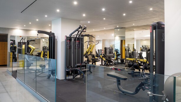 Une salle de sport moderne dotée de divers appareils d’exercice, de murs en verre et d’un intérieur propre et bien éclairé.
