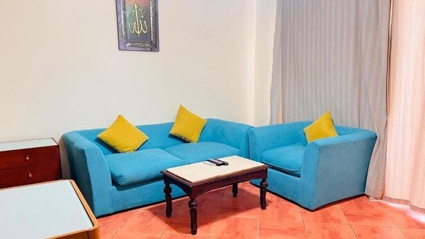 A living room with a blue sofa set, two yellow cushions, a wooden coffee table, and a framed religious text on the wall. - Porto Golf Marina Apartments (El Alamein)