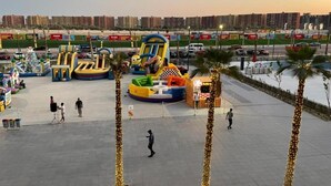 An outdoor amusement area with inflatable rides, palm trees, and a parking lot. - Porto Golf Marina Apartments (El Alamein)
