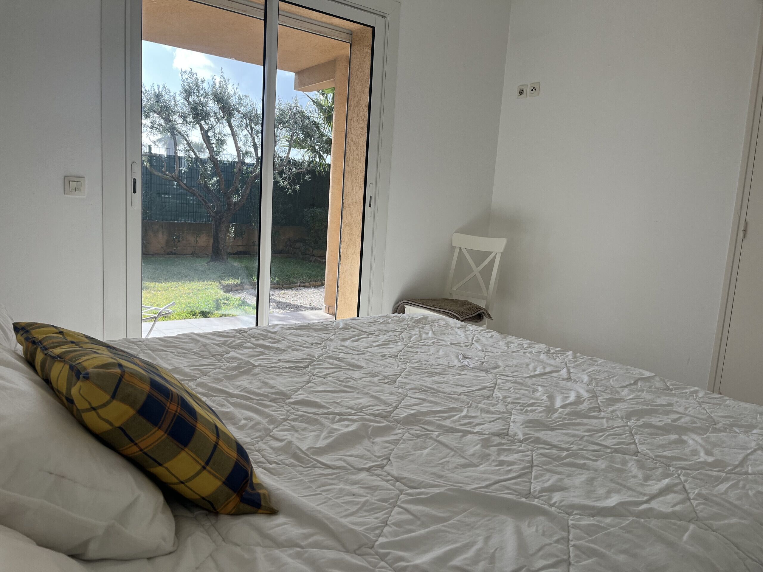 A bedroom with a bed, a chair, and a view of the outdoors through a sliding door.