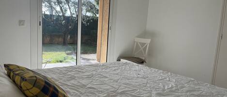 A bedroom with a bed, a chair, and a view of the outdoors through a sliding door.