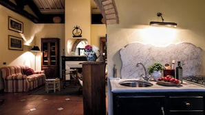 A cozy living room with a sofa, a wooden cabinet, and a dining area with a table and chairs. A kitchen area with a marble countertop and sink is visible. - Cottage on the Chianti Hills-Il Borghetto (San Casciano In Val Di Pesa)