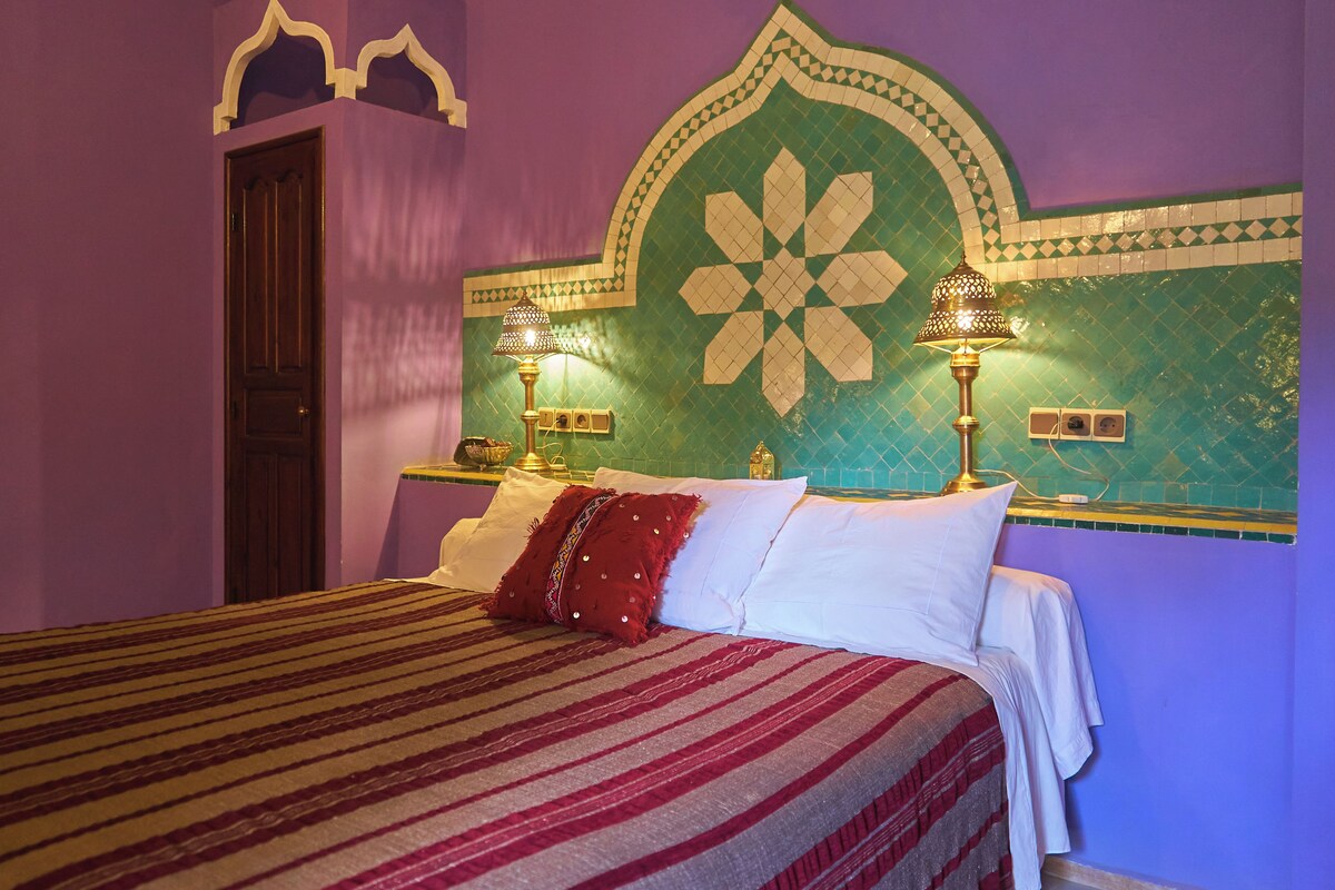 Un lit avec une couvre-lit à rayures, deux lampes de chevet et un mur décoratif orné d’un motif géométrique.