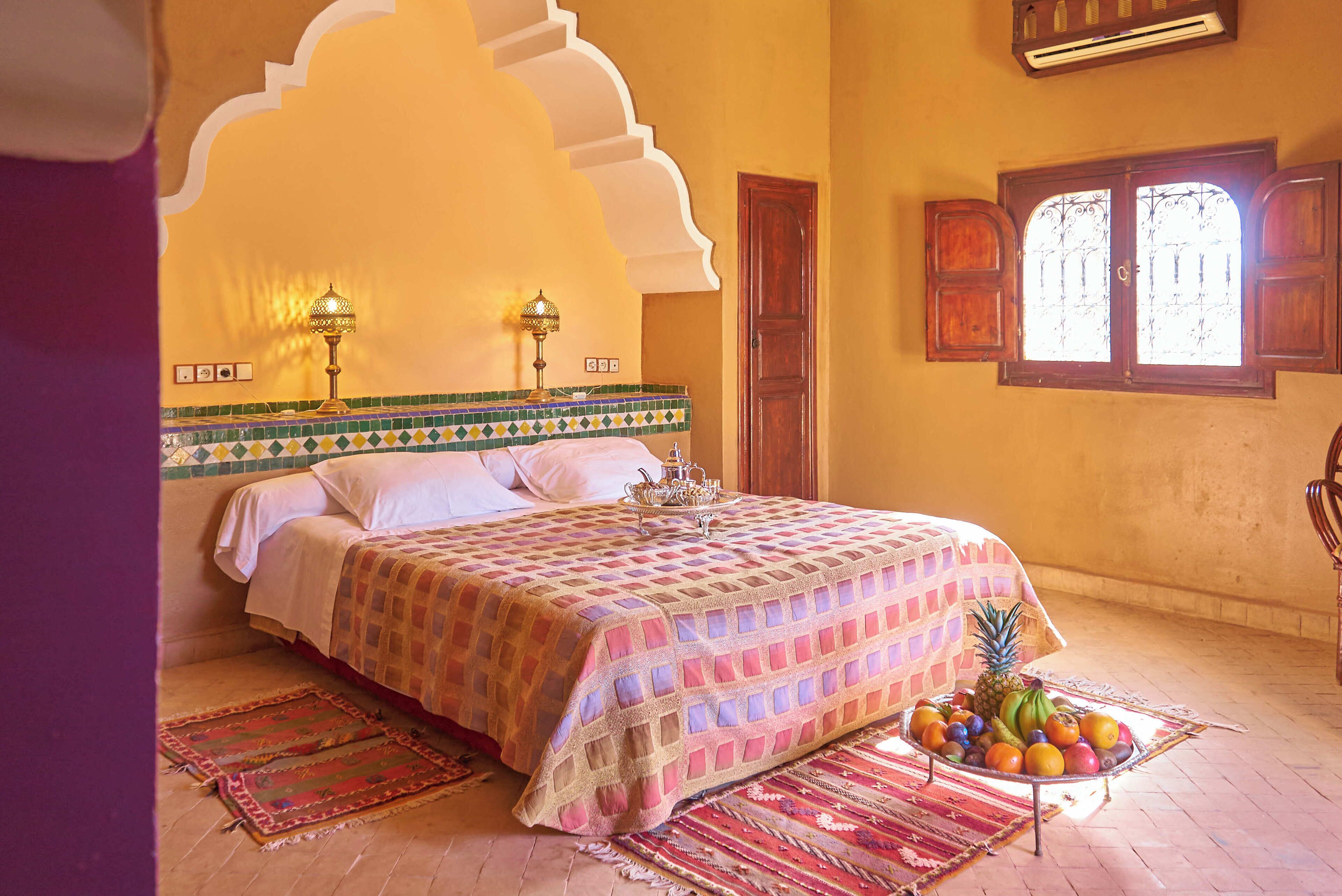 A bedroom with a bed, a fruit bowl, and a window with decorative shutters.